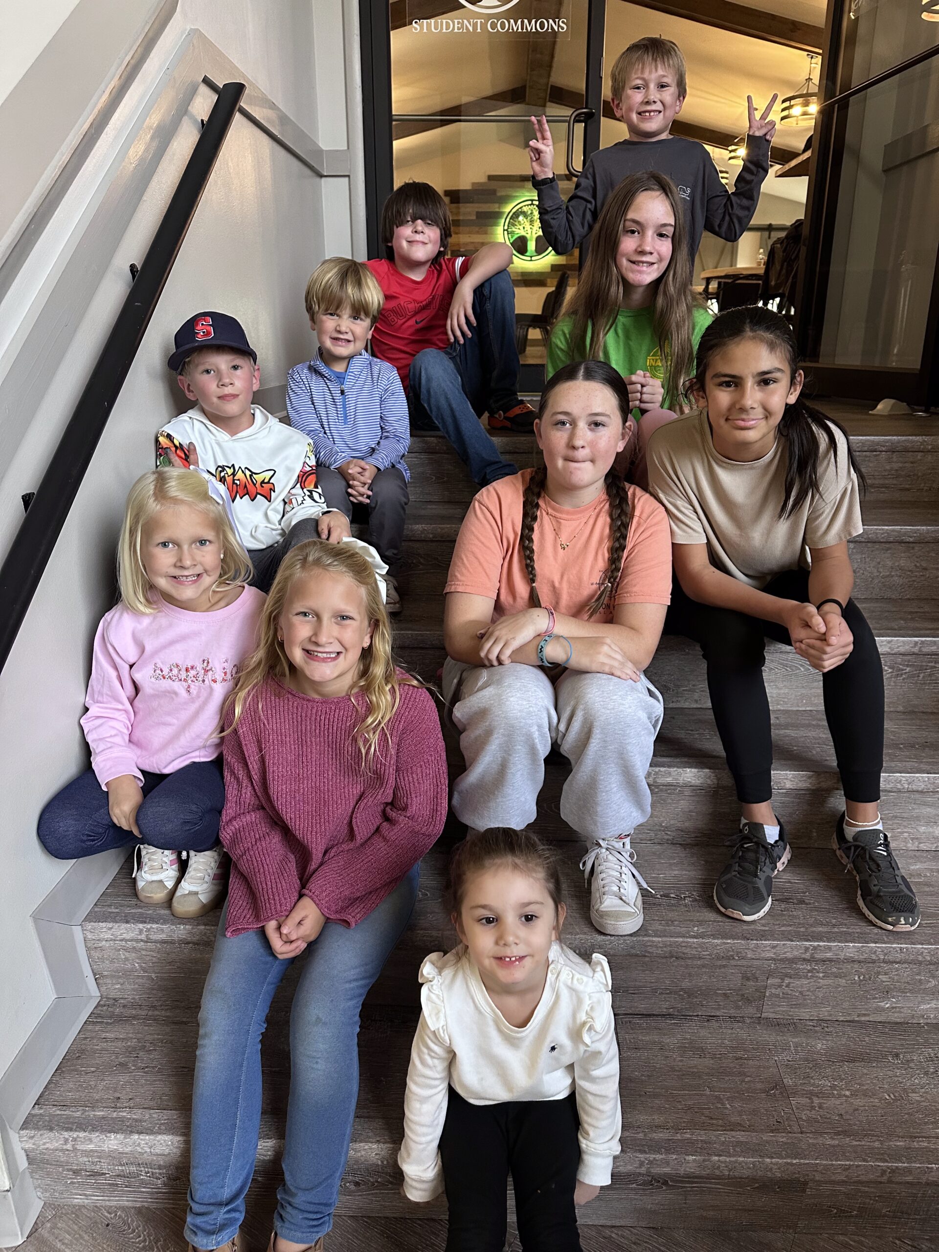 a group of kids aged 5-10 sitting on stairs indoors